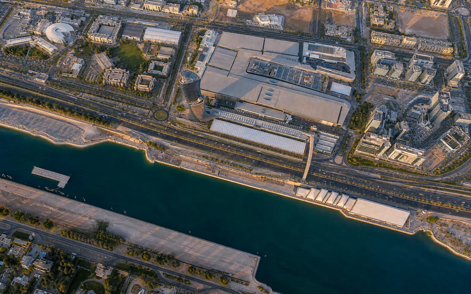Aerial view of ADNEC Centre Abu Dhabi, its exhibition halls, and the waterfront surrounding the firm's location.